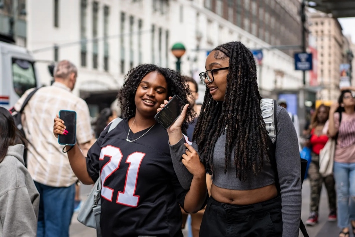 Mujeres con sus teléfonos móviles en la ciudad de Nueva York, el 10 de junio de 2024. Los expertos afirman que las redes sociales sirven de foro para grupos que promueven la violencia, a pesar de las restricciones de las plataformas. (Samira Bouaou/The Epoch Times)
