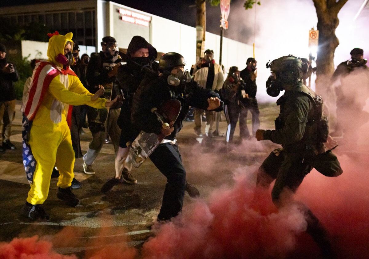 Un manifestante antifa devuelve una bomba de humo a los agentes federales frente a las oficinas del Servicio de Inmigración y Control de Aduanas en Portland, Oregón, el 5 de octubre de 2025. (John Fredricks/The Epoch Times).