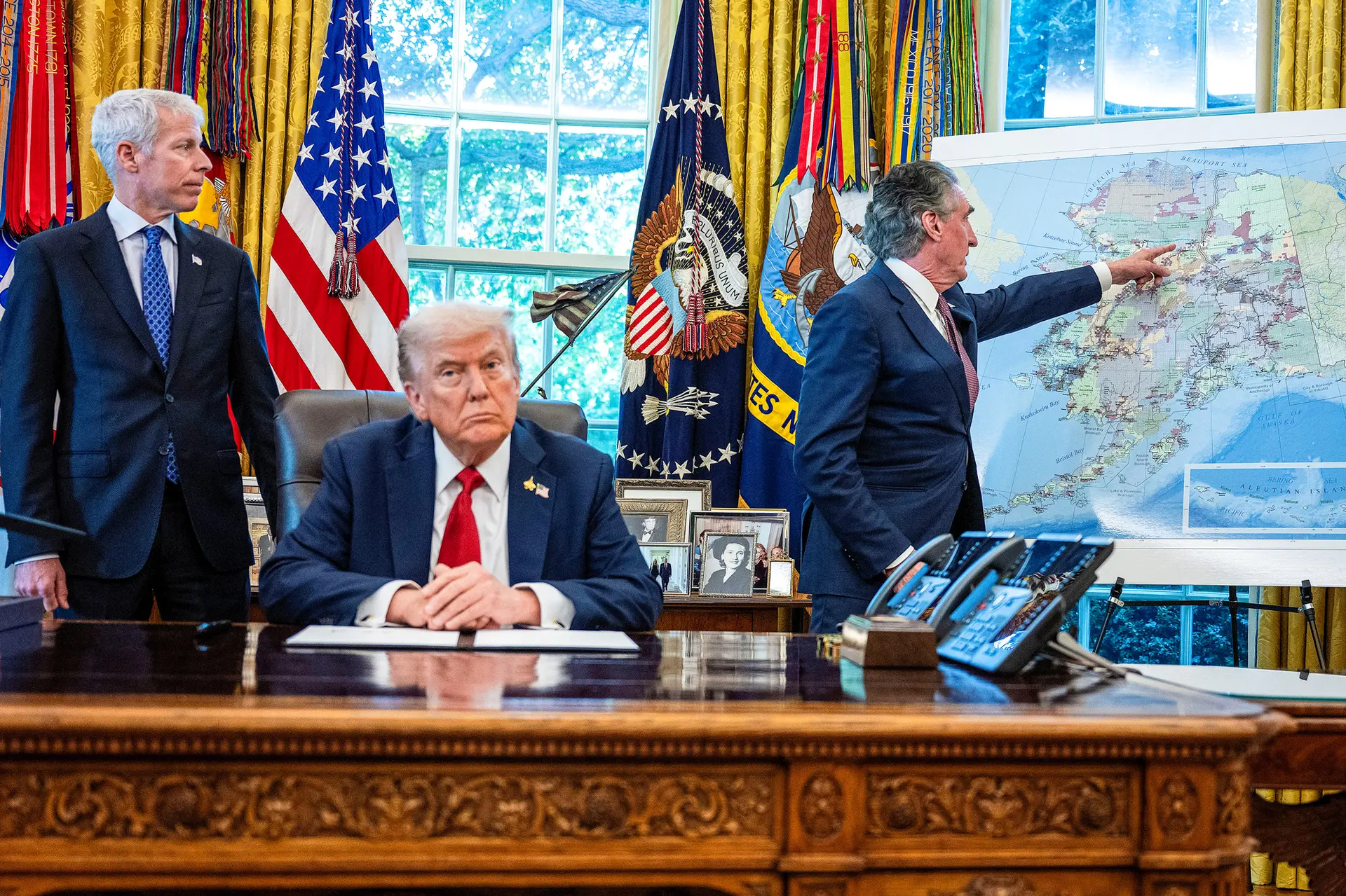 El presidente Donald Trump escucha mientras el secretario del Interior, Doug Burgum (derecha), señala un mapa de Alaska y el secretario de Energía, Chris Wright (izquierda), observa, después de que Trump firmara una orden ejecutiva para autorizar el proyecto minero Ambler Road en Alaska, en el Despacho Oval, el 6 de octubre de 2025. (Jim Watson/AFP a través de Getty Images).