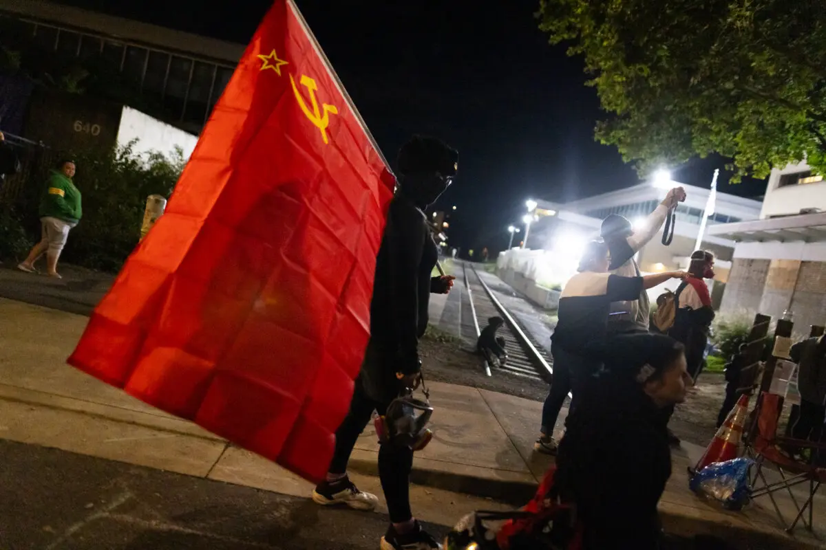 Una mujer lleva una bandera comunista frente a las oficinas del Servicio de Inmigración y Control de Aduanas en Portland, Oregón, el 4 de octubre de 2025. (John Fredricks/The Epoch Times)