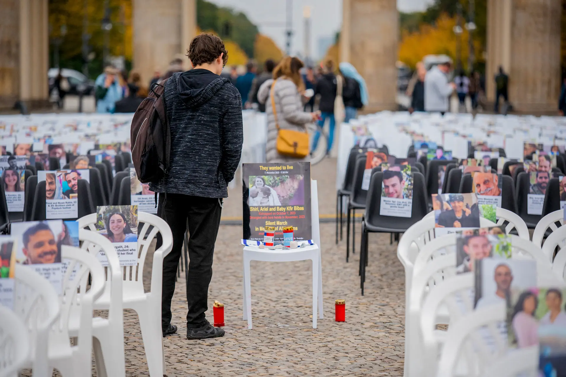 <em>Personas visitan filas de sillas vacías con fotos de víctimas y rehenes israelíes, expuestas durante una vigilia conmemorativa frente a la Puerta de Brandeburgo en Berlín el 7 de octubre de 2025. La instalación, con más de 1000 sillas, fue organizada por la Unión de Estudiantes Judíos de Alemania para conmemorar a las víctimas del ataque de Hamás contra Israel del 7 de octubre de 2023. (Stefan Frank/Middle East Images/AFP vía Getty Images)</em>