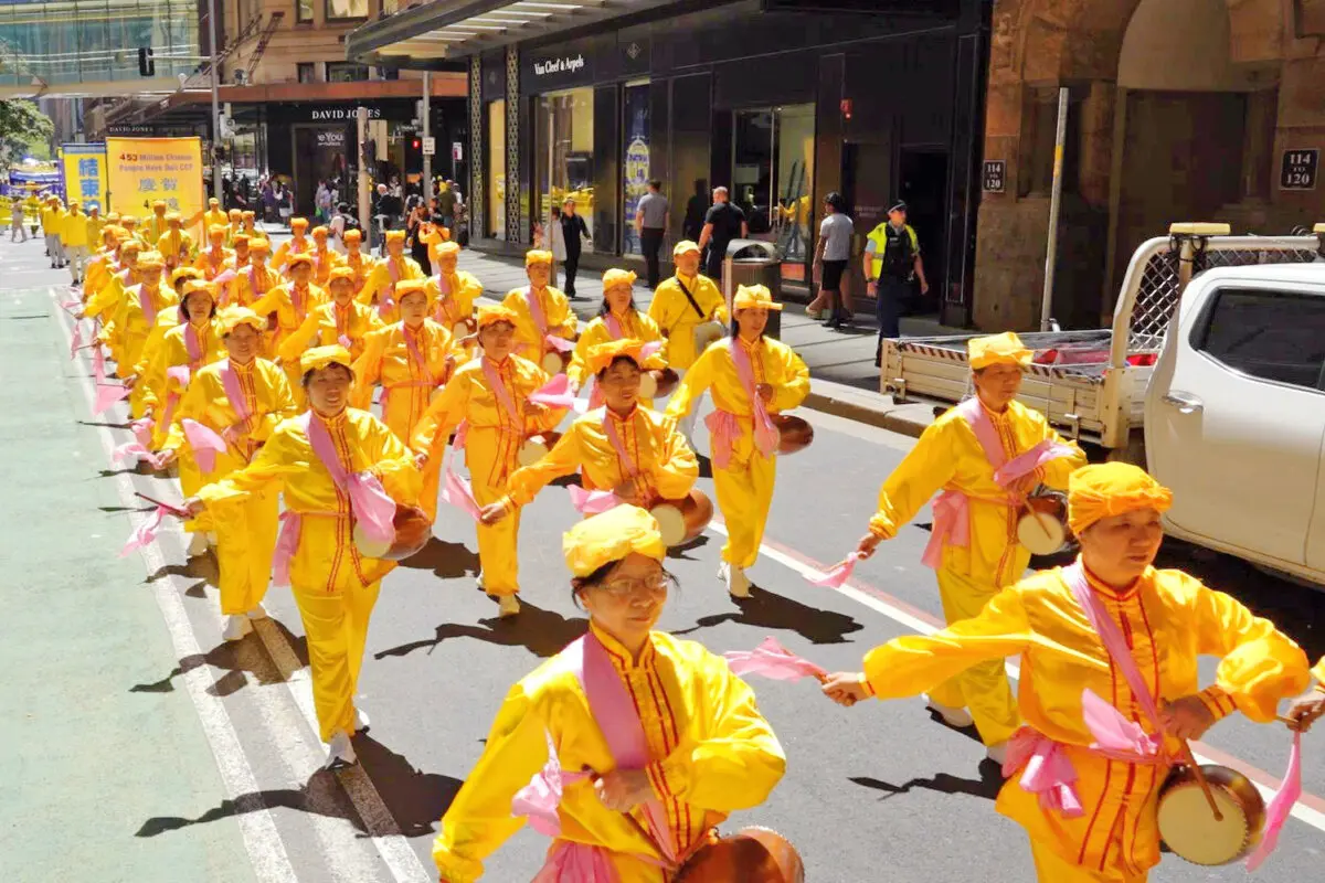 Practicantes de Falun Dafa vestidos con trajes tradicionales chinos con tambores de cintura actúan durante un desfile por el concurrido distrito financiero de Sídney, Australia, el 10 de octubre de 2025. (Wang Nan/NTD TV).