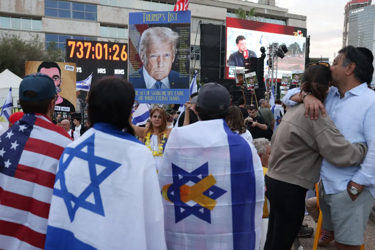 <em>Personas envueltas en banderas estadounidenses e israelíes rodean un retrato del presidente de EE. UU. Donald Trump mientras esperan la liberación de los rehenes israelíes de Gaza en la Plaza de Rehenes en Tel Aviv el 13 de octubre de 2025. (Ahmad Gharabli/AFP vía Getty Images)</em>
