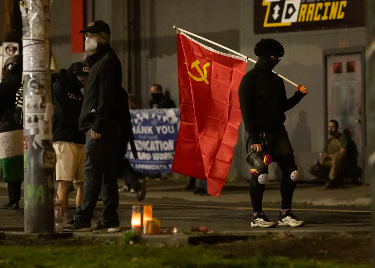 <em>Una mujer porta una bandera comunista frente a las oficinas del Servicio de Inmigración y Control de Aduanas en Portland, Oregón, el 4 de octubre de 2025. (John Fredricks/The Epoch Times)</em>
