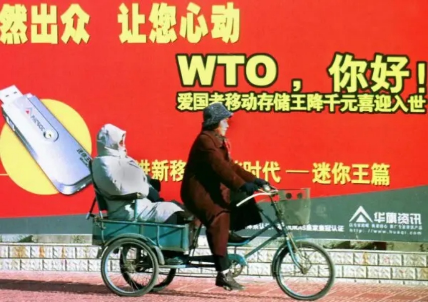 Una pareja montada en un triciclo frente a una valla publicitaria que da la bienvenida a China como miembro de la Organización Mundial del Comercio (OMC), en Beijing, el 23 de diciembre de 2001. (AFP a través de Getty Images)