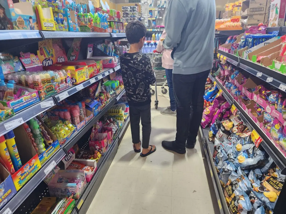 Un niño junto a su padre en la cola de la caja de un supermercado de Albany, Australia Occidental, el 7 de septiembre de 2024. La caja está llena de comida basura con envoltorios de colores dirigida al público infantil. Susan Mortimer/The Epoch Times