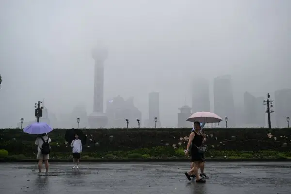<em>Personas caminan por el paseo marítimo del Bund a lo largo del río Huangpu durante el paso del tifón Co-May en Shanghái el 30 de julio de 2025. (Héctor Retamal/AFP vía Getty Images)</em>