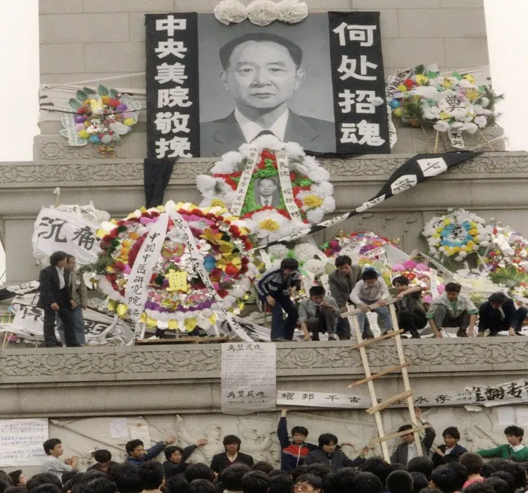 Los estudiantes colocan flores y coronas de flores frente al retrato del antiguo líder del PCCh y reformista liberal Hu Yaobang, mientras miles de estudiantes se reúnen al pie del monumento a los Héroes del Pueblo en la plaza de Tiananmen durante una manifestación no autorizada en Beijing, el 19 de abril de 1989. (Catherine Henriette/AFP/Getty Images)