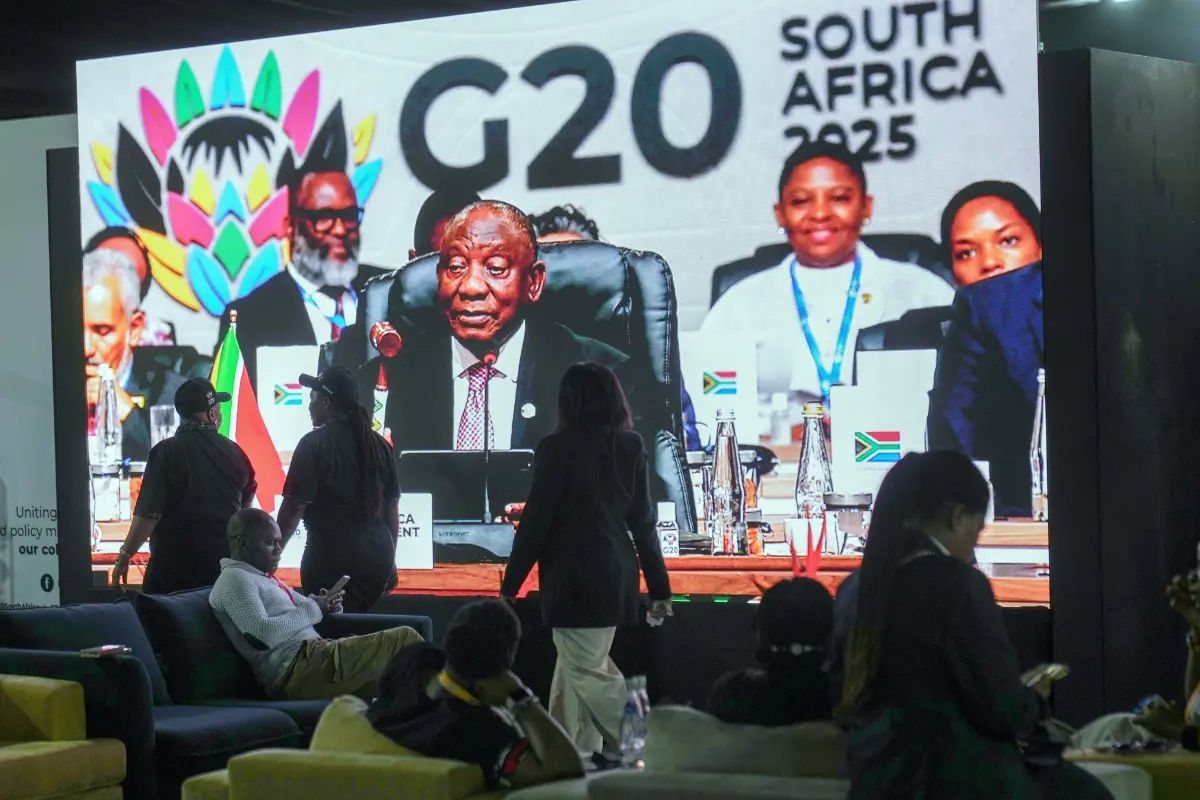La gente pasa junto a una gran pantalla de televisión en la que el presidente sudafricano Cyril Ramaphosa sostiene un mazo de madera mientras clausura oficialmente la cumbre de líderes del G20, en Johannesburgo, Sudáfrica, el 23 de noviembre de 2025. (Jerome Delay/AP Photo)