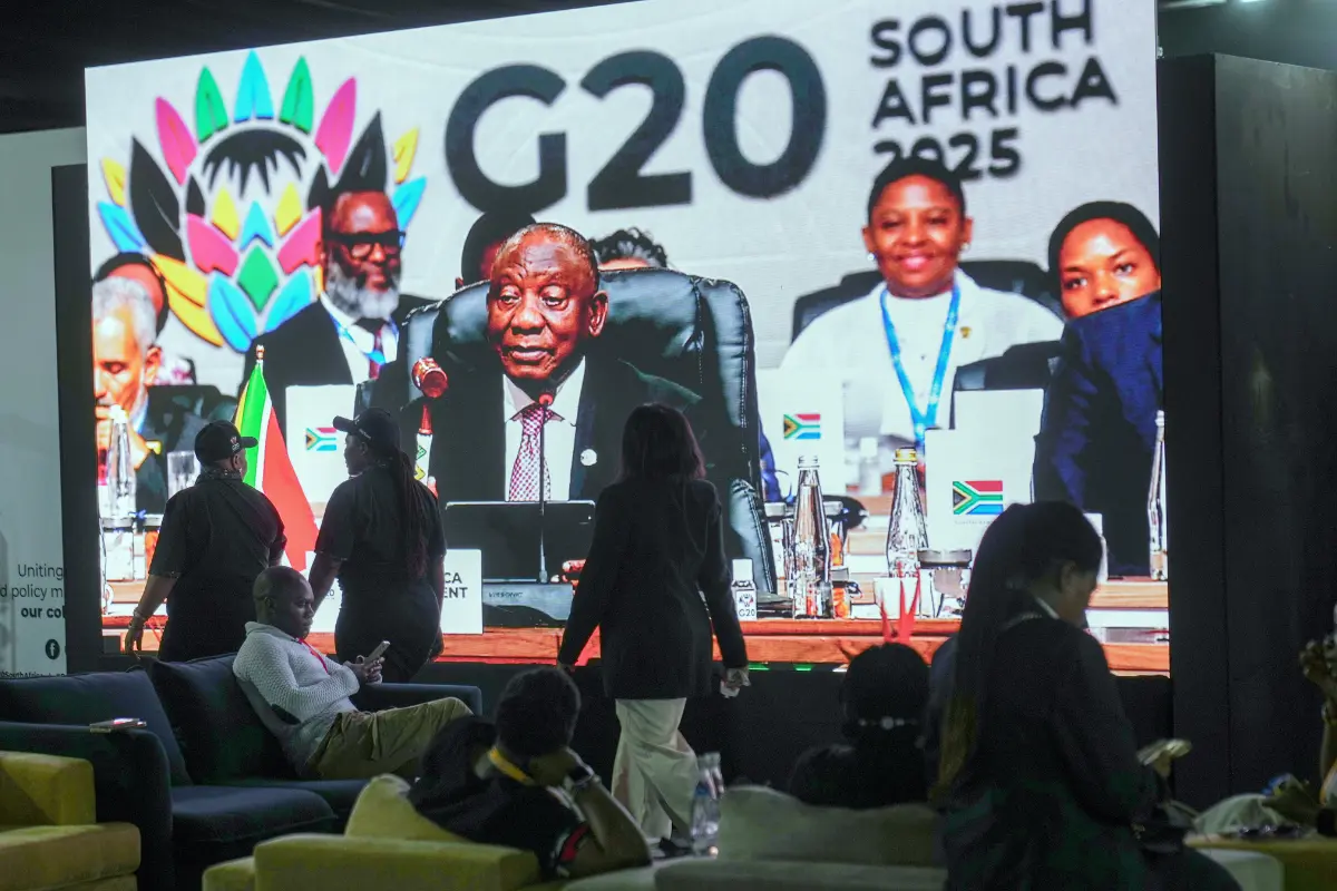 <em>La gente pasa junto a un televisor de pantalla gigante donde el presidente sudafricano Cyril Ramaphosa sostiene un mazo de madera mientras clausura oficialmente la cumbre de líderes del G20, en Johannesburgo, el 23 de noviembre de 2025. (Jerome Delay/Foto AP Jerome Delay/Foto AP)</em>