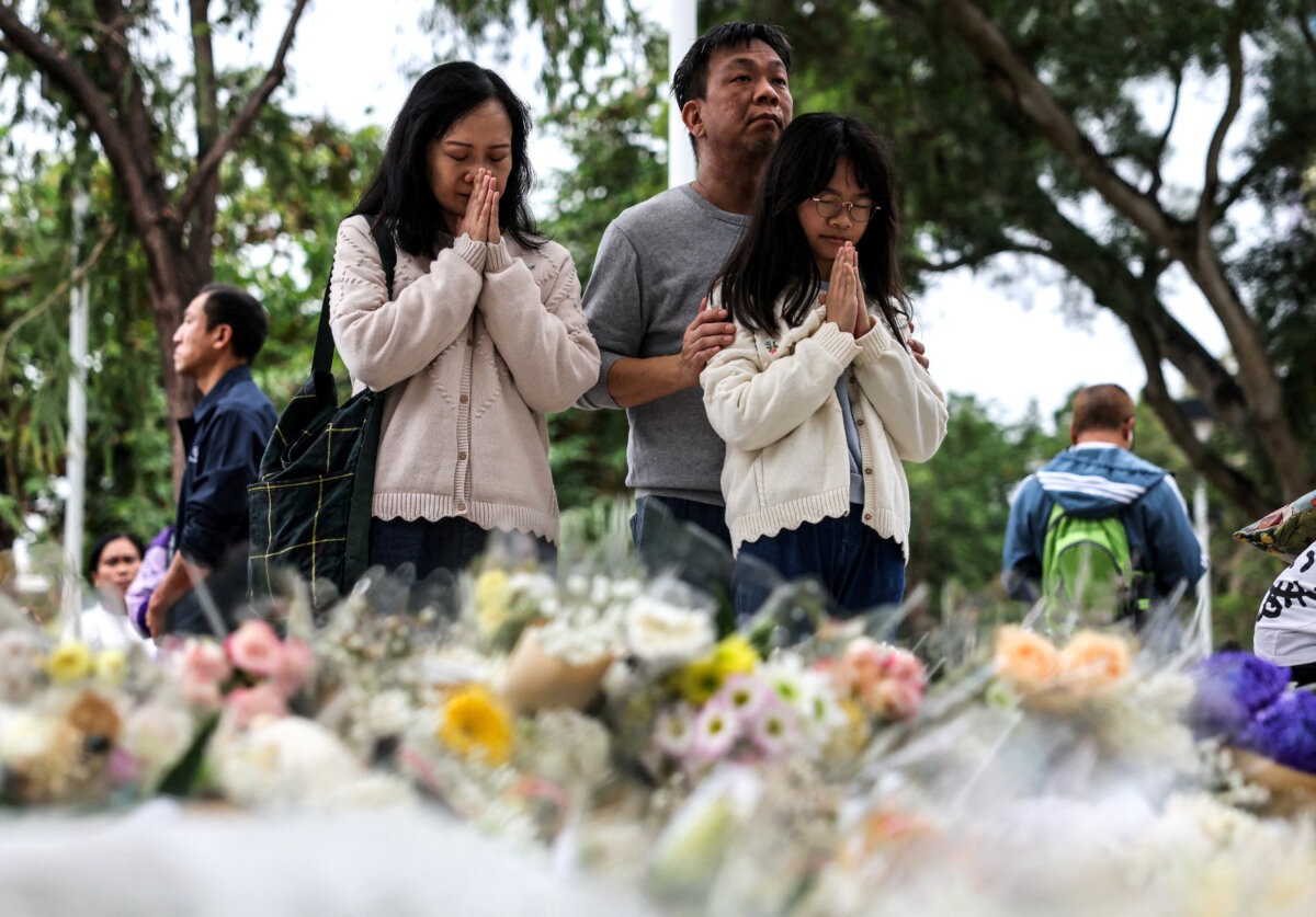 La gente reza mientras deposita flores en el memorial improvisado en memoria de las víctimas del mortal incendio del complejo residencial Wang Fuk Court, en Tai Po, Hong Kong, el 30 de noviembre de 2025. (Maxim Shemetov/Reuters).